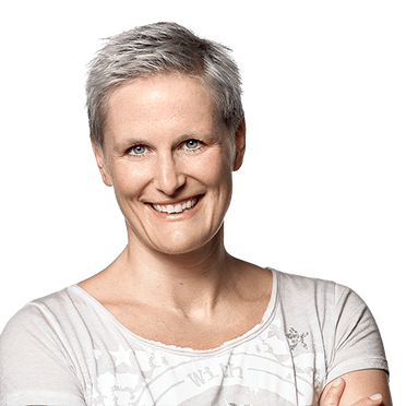 Nina Schulze steht vor einem grünen Hintergrund und lächelt, sie trägt ein weißes T-Shirt.