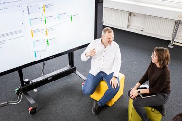 Zwei Personen sitzen vor einem interaktiven Bildschirm mit einer grafischen Darstellung eines Geschäftsprozesses. Diskussion über Digitalisierungs-Werkzeuge für Geschäftsprozesse.