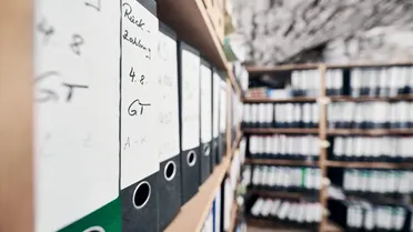 Regal mit Aktenordnern, die archivierte E-Mails und Dokumente enthalten, relevant für revisionssichere Archivierung. Lösung zur Digitalisierung von Dokumenten.