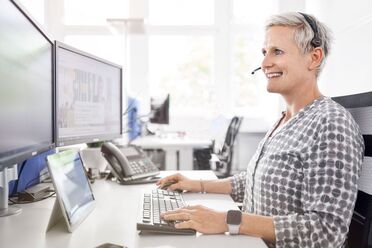 Nina Schulze arbeitet an ihrem Schreibtisch mit mehreren Monitoren und einem Headset, zeigt die Digitalisierungs-Werkzeuge im Einsatz.