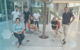 Das Team der Syxos GmbH aus München steht und sitzt um einen Baum in der Büro-Lobby, die moderne IT-Lösungen entwickelt.