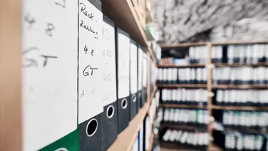 Regal mit Aktenordnern, die archivierte E-Mails und Dokumente enthalten, relevant für revisionssichere Archivierung. Lösung zur Digitalisierung von Dokumenten.