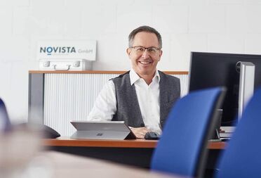 Hans-Ulrich Stämpfli sitzt am Schreibtisch bei Novista GmbH mit einem Tablet und einem Computer im Hintergrund.