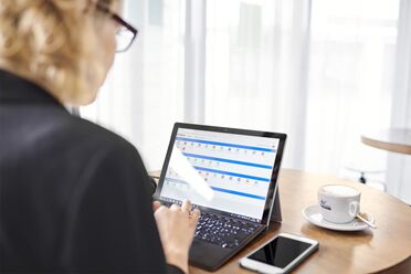 Ein Mitarbeiter von agorum Software GmbH arbeitet an einem Laptop im Café, während ein Cappuccino auf dem Tisch steht.