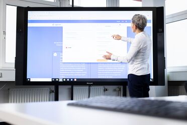 Eine Mitarbeiterin zeigt auf einem großen Bildschirm die Möglichkeiten der digitalen Transformation für Unternehmen.
