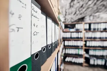 Regal mit Aktenordnern, die archivierte E-Mails und Dokumente enthalten, relevant für revisionssichere Archivierung. Lösung zur Digitalisierung von Dokumenten.