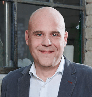 Lukas Amrein von Data Dynamic Informatic steht vor einem Fenster im Büro, er trägt ein weißes Hemd und einen dunklen Blazer.