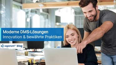 Zwei Mitarbeiter arbeiten zusammen an einem Laptop in einem modernen Büro, um Dokumentenmanagement-Systeme (DMS) zu optimieren.