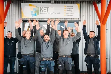 Team der Küstenhaus Energie Technik GmbH jubelt vor Firmengebäude. Photovoltaik und Elektrotechnik Spezialisten.