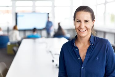 Anne Klein, Geschäftsführerin von agorum Software, steht in einem modernen Büro mit einem großen Konferenztisch und einem Bildschirm im Hintergrund.