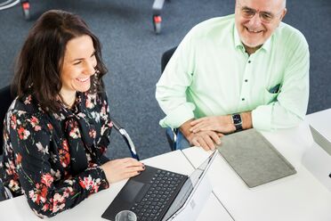 Zwei Personen arbeiten an einem Tisch mit einem Laptop, das zeigt die Integration von SAP Dokumentenmanagement mit einem DMS.