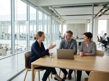 Drei Personen in einer Arbeitsbesprechung an einem hellen Besprechungstisch