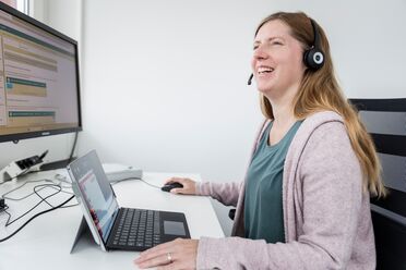 Eine Mitarbeiterin namens Daniela Lutz arbeitet an ihrem Schreibtisch mit einem Laptop und einem Monitor, die das Dokumentenmanagement-System anzeigen.