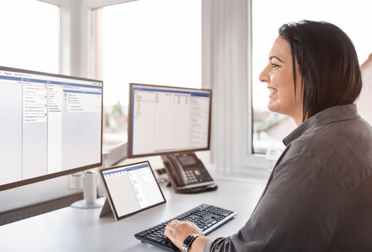 Mitarbeiterin arbeitet an mehreren Monitoren mit dem agorum core Interface, zeigt digitalen Workplace.