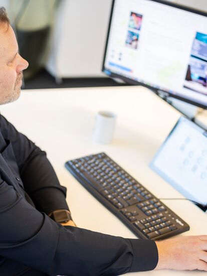 Ein Mitarbeiter arbeitet an einem Schreibtisch mit mehreren Monitoren, die das Dokumentenmanagement-System anzeigen.