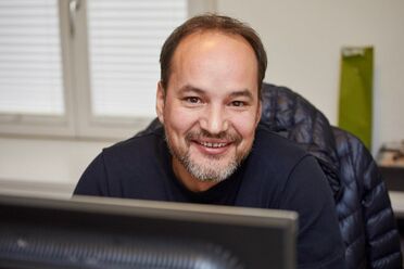 Gian-Andrea Prevost sitzt an einem Schreibtisch mit Computer im Büro der Firma Romano Christen Schweiz.