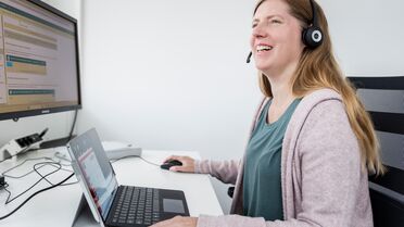 Eine Mitarbeiterin namens Daniela Lutz arbeitet an ihrem Schreibtisch mit einem Laptop und einem Monitor, die das Dokumentenmanagement-System anzeigen.