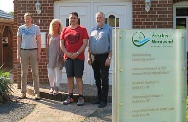 Das Team von Frischer Nordwind steht vor einem Gebäude, neben einem Schild mit Firmeninformationen.