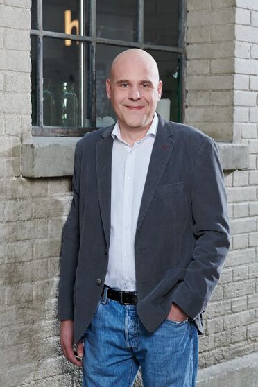 Lukas Amrein steht vor einer Backsteinwand und trägt einen grauen Blazer, ein weißes Hemd und Jeans. Er ist IT-Experte bei Data Dynamic Informatic AG, die Schweizer KMUs zu ERP-Lösungen berät.