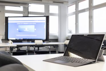 Ein Büro mit einem Laptop im Vordergrund und einem Bildschirm im Hintergrund, der Schnittstelleninformationen für Dokumentenmanagement zeigt.