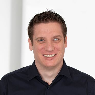 Daniel Bachinger, Mitarbeiter der Swiss Helicopter Group, trägt ein dunkles Hemd vor weißem Hintergrund.