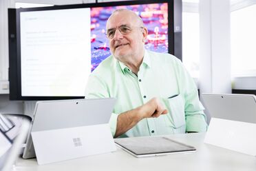 Ein agorum Partner sitzt an einem Tisch mit mehreren Microsoft Surface-Geräten und zeigt auf ein Dokument, während im Hintergrund ein Bildschirm Informationen zum Dokumentenmanagement anzeigt.