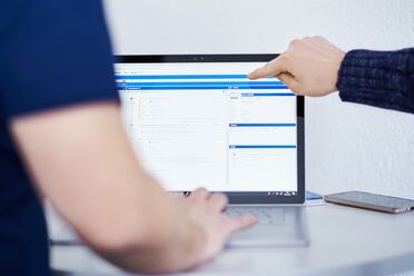 Ein Mitarbeiter zeigt auf das Dashboard eines Open Source DMS auf einem Laptop, das verschiedene Dokumentenmanagement-Funktionen anzeigt.