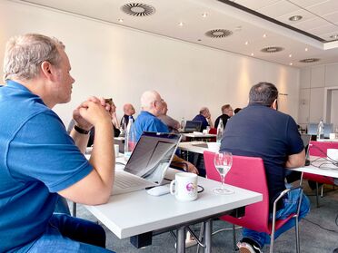 Teilnehmer sitzen an Tischen mit Laptops und diskutieren im Rahmen des Partner-Tags 2024 von agorum core pro.