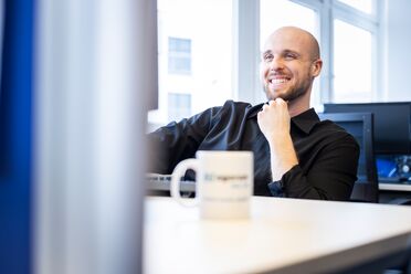 Ein IT-Administrator sitzt am Schreibtisch im Büro und hält eine Tasse mit dem Logo von agorum Software GmbH.