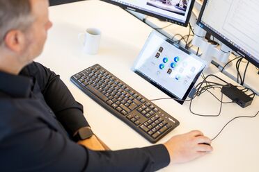 Ein IT-Administrator arbeitet an einem Schreibtisch mit mehreren Monitoren und einem Tablet, das das Dokumentenmanagement-System zeigt.