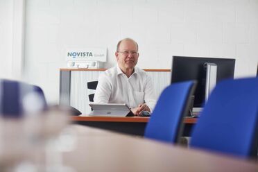 Martin Lauper sitzt am Schreibtisch im Büro von NOVISTA GmbH mit einem Laptop und einem Computerbildschirm im Hintergrund.