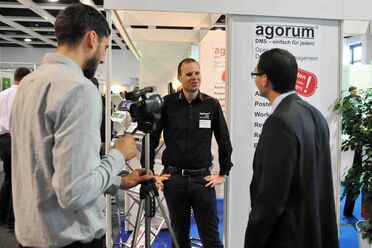 Oliver Schulze wird auf der Messe von einem Kameramann interviewt, während ein Besucher zuhört.