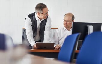 Zwei Mitarbeiter der NOVISTA GmbH diskutieren an einem Schreibtisch mit einem Tablet über Geschäftsprozesse.