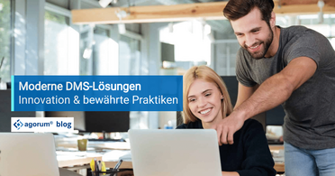 Zwei Mitarbeiter arbeiten zusammen an einem Laptop in einem modernen Büro, um Dokumentenmanagement-Systeme (DMS) zu optimieren.