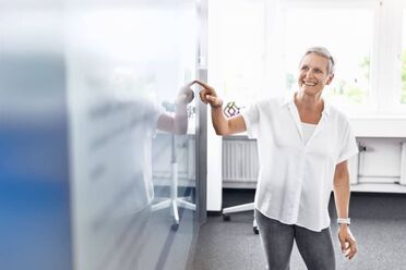 Nina Schulze zeigt auf ein Whiteboard in einem modernen Büro, das digitale Transformation und agile Arbeitsweisen darstellt.