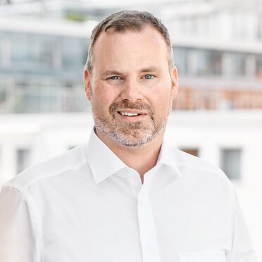Porträt von Oliver Schulze, Geschäftsführer, vor einem modernen Bürogebäude