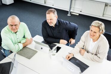 Drei Mitarbeiter arbeiten zusammen an einem Tisch mit Laptops und nutzen ECM-Software für Social Collaboration.